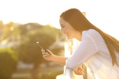 Bir akıllı telefon günbatımında bir balkonda kullanan kadın