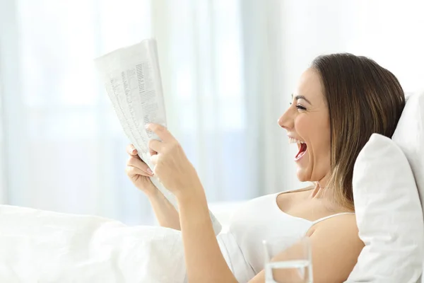 Mulher excitada lendo um jornal na cama — Fotografia de Stock