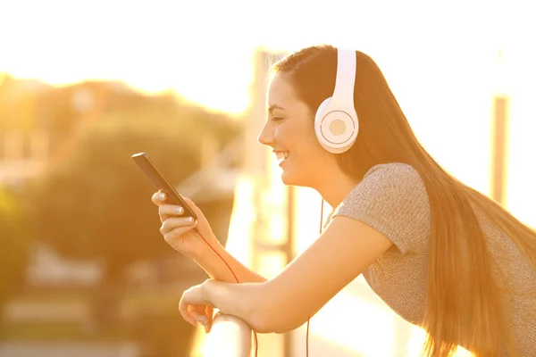 Meisje muziek beluisteren bij zonsondergang in een balkon — Stockfoto