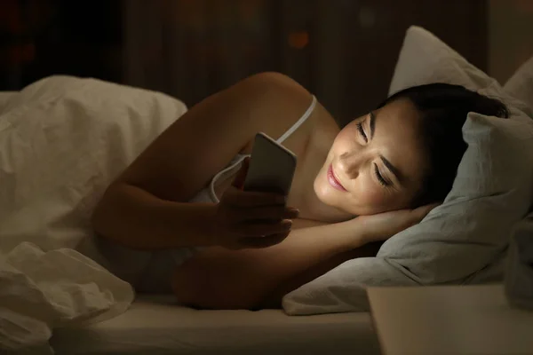 Gadis itu menggunakan ponsel pintar di tempat tidur di malam hari — Stok Foto