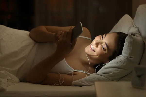 夜にベッドの上の音楽を聴いて幸せな女の子 — ストック写真