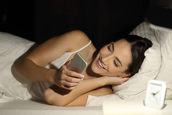 Šťastná dívka pomocí chytrého telefonu na posteli v noci — Stock fotografie