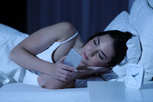 Wanita serius menggunakan telepon pintar di malam hari di tempat tidur — Stok Foto