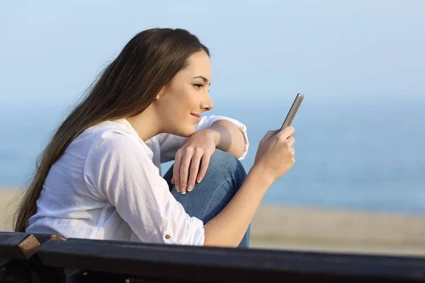 Розслаблена дівчина дивиться вміст телефону на пляжі — стокове фото