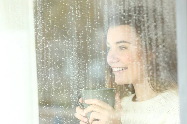 Adolescente sorridente che guarda attraverso una finestra in un giorno di pioggia — Foto Stock