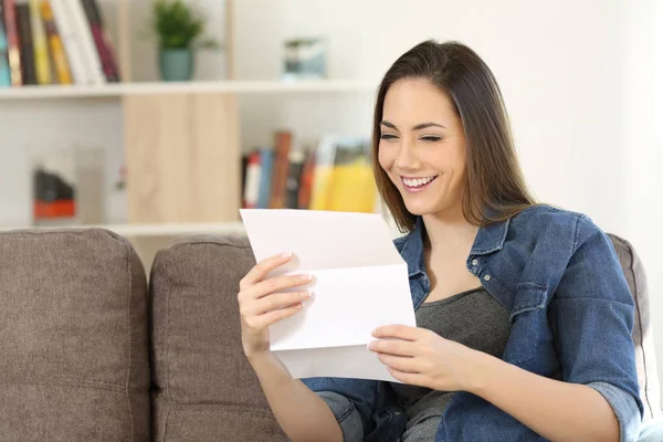 Mujer feliz leyendo una carta en un sofá en casa —  Fotos de Stock