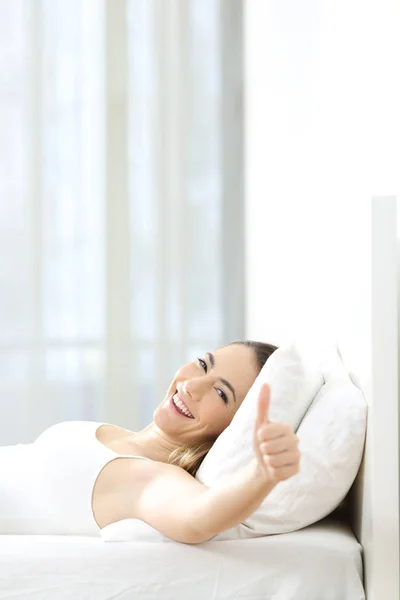 Woman gesturing thumbs up lying on a bed — Stock Photo, Image