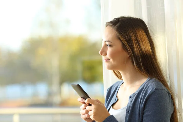 Mujer usando un teléfono inteligente mirando al aire libre en casa — Foto de Stock