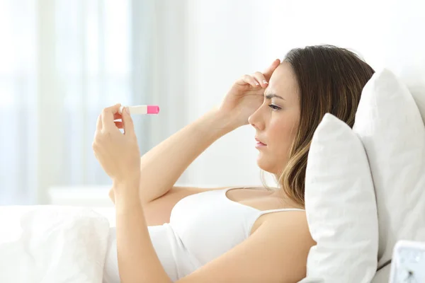 Mujer preocupada revisando una prueba de embarazo en la cama —  Fotos de Stock