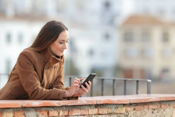 Poważna kobieta korzystająca z telefonu komórkowego w zimie na balkonie — Zdjęcie stockowe