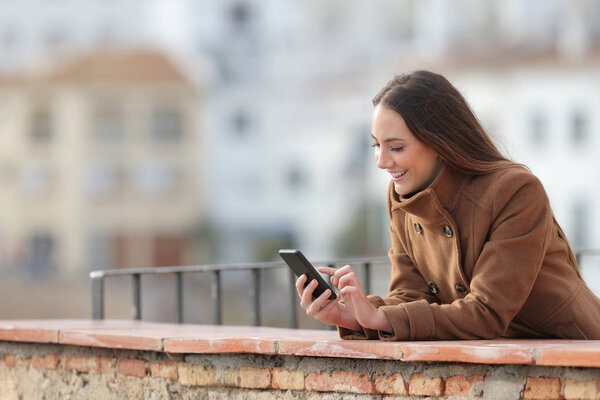 Счастливая женщина с мобильным телефоном зимой на балконе
