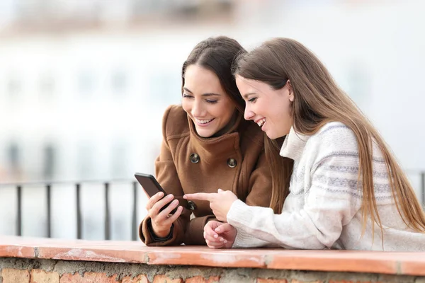 Dois amigos felizes verificando celular no inverno — Fotografia de Stock