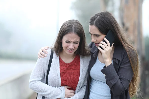 Chica sufriendo dolor de vientre y un amigo llamando a la asistencia — Foto de Stock