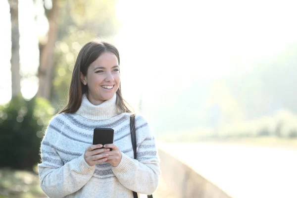 Menina feliz com suéter mantém o telefone olhando para longe — Fotografia de Stock