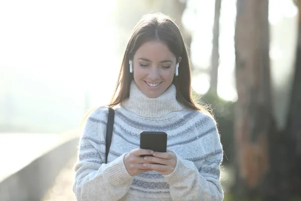 Щаслива жінка взимку використовує мобільний телефон, що йде в парку — стокове фото