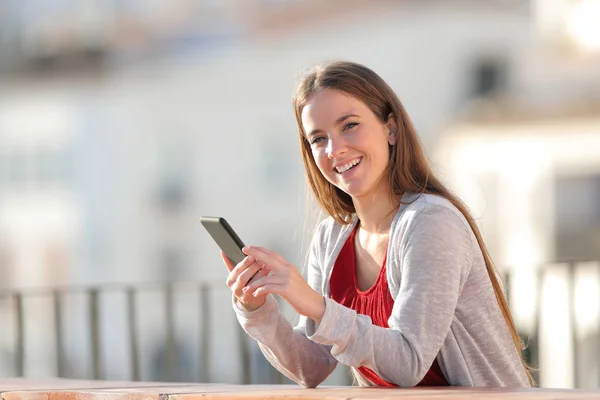 Femme heureuse regarde la caméra tenant le téléphone dans un balcon — Photo