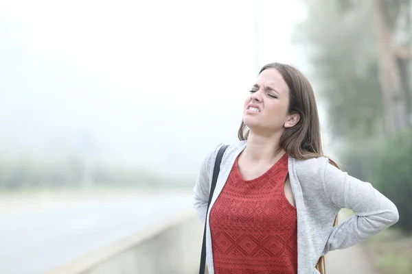 Mujer sufriendo dolor de espalda un día de niebla fría — Foto de Stock