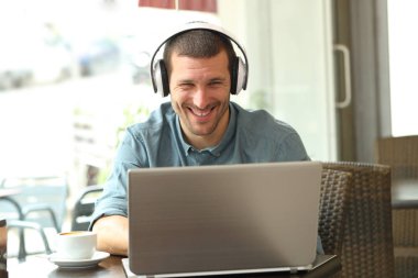 Barda kulaklıklı dizüstü bilgisayar kullanan mutlu bir adam.