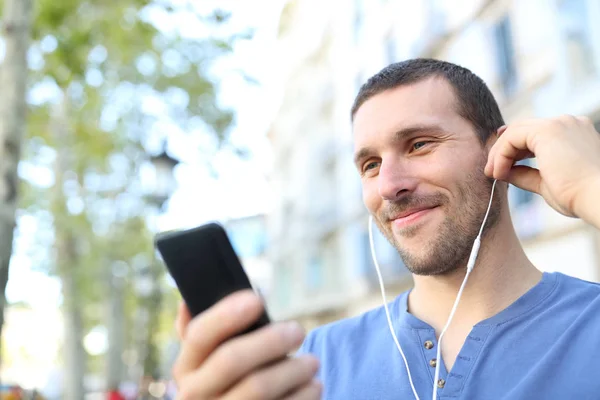 Satisfied adult man listening to music with earbuds in the street — Stock Photo, Image