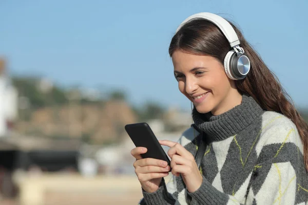 Gelukkig meisje luisteren naar muziek met behulp van mobiele telefoon in de winter — Stockfoto