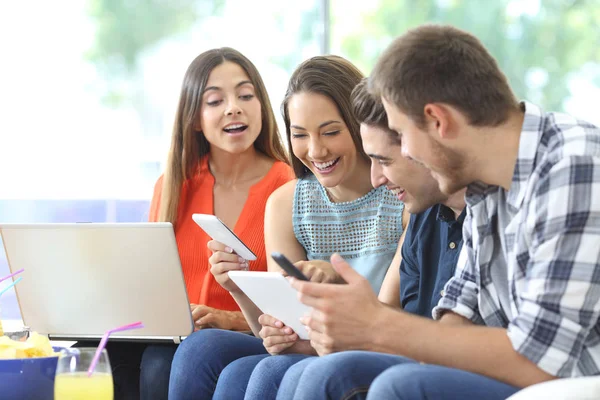 Cuatro amigos felices revisando múltiples dispositivos en casa — Foto de Stock