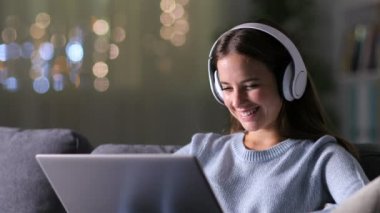 Kulaklıklı mutlu kadın evdeki kanepede oturmuş dizüstü bilgisayarını kontrol ediyor. 