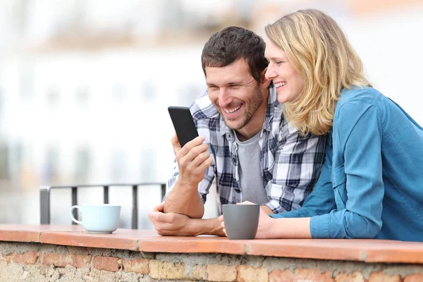 Feliz pareja adulta revisando el teléfono inteligente en un balcón — Foto de Stock