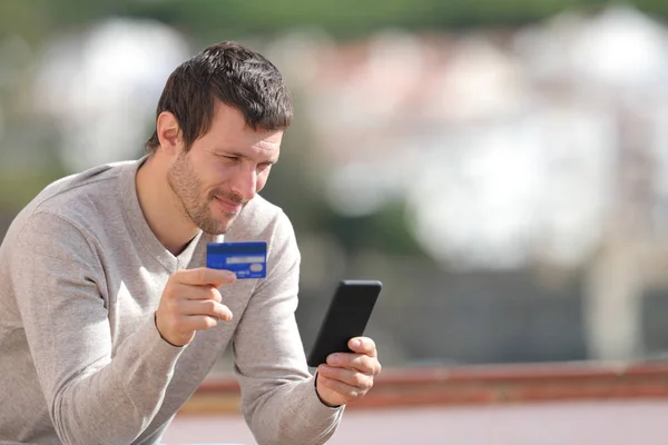 Homem sério comprando online com cartão de crédito e telefone — Fotografia de Stock