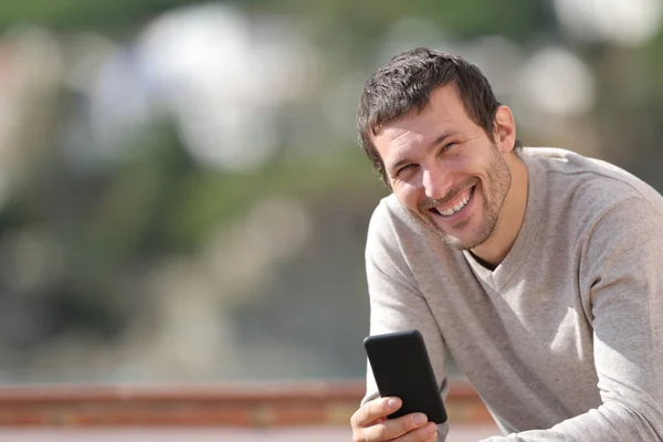 Homem adulto feliz segurando telefone inteligente olha para a câmera — Fotografia de Stock