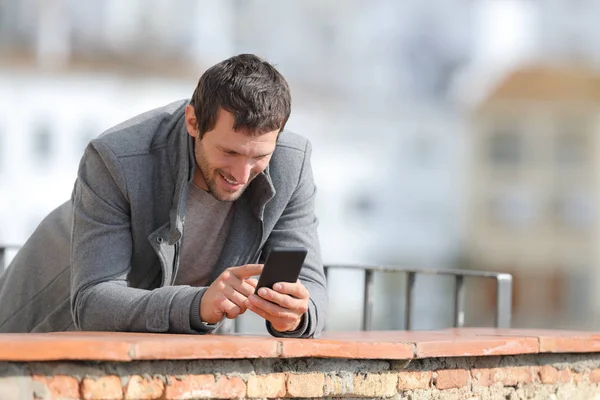 Homem feliz no inverno usando telefone celular em uma varanda — Fotografia de Stock
