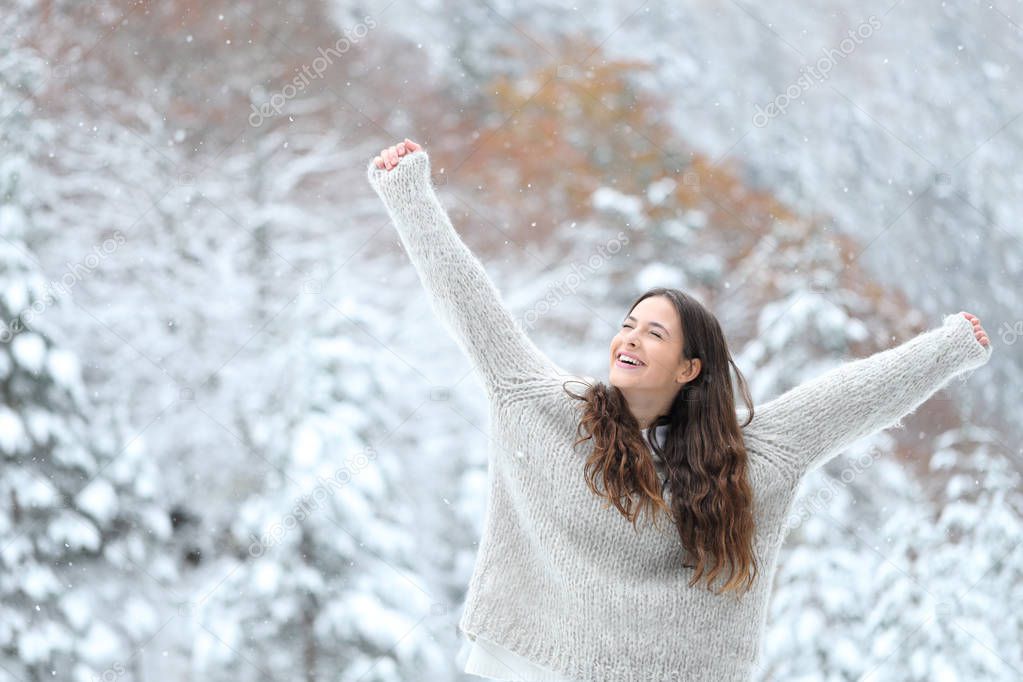 Excited girl enjoying snow in winter raising arms