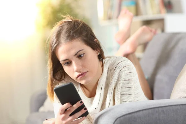 Serious girl using mobile phone lying on a couch — Stock Photo, Image