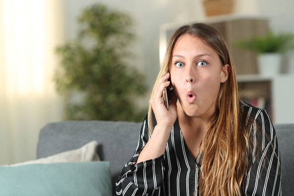 Surprised woman talking on phone looks at camera