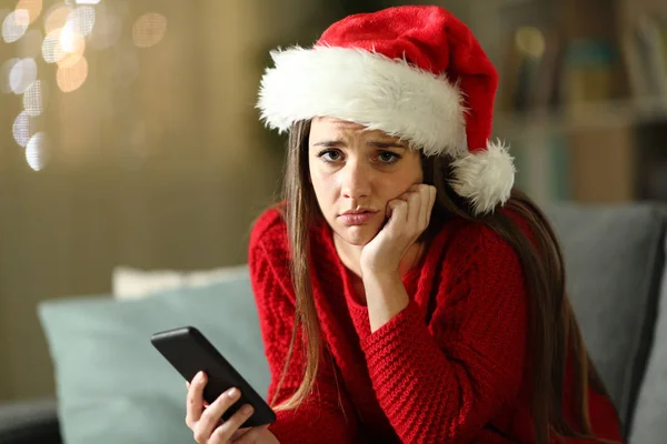 Сумна жінка тримає телефон вдома на різдвяні канікули — стокове фото