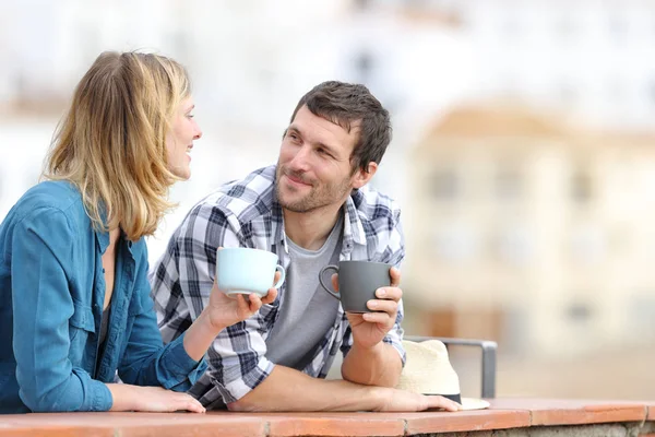 Relajada pareja hablando sosteniendo tazas en un balcón — Foto de Stock