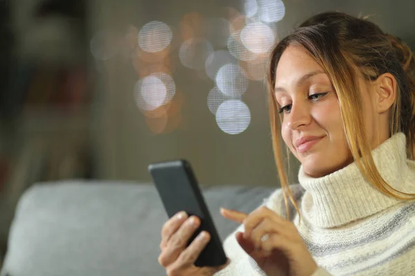 Mujer en invierno revisando el teléfono móvil en casa en la noche — Foto de Stock