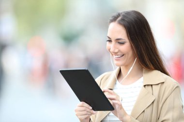 Sokakta tablet kullanan kulaklık takan mutlu bir kadın.