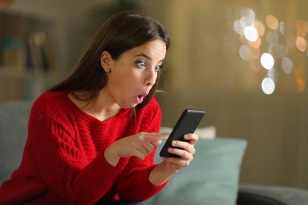 Удивлённая женщина в красном проверяет смартфон ночью — стоковое фото