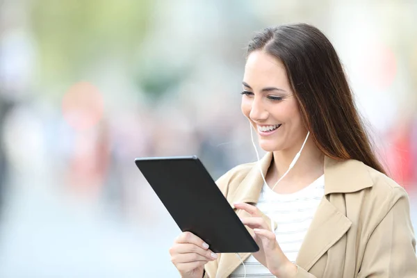 Šťastná žena nosí sluchátka pomocí tabletu na ulici — Stock fotografie