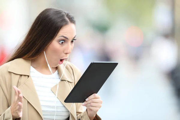 Verrast vrouw met oortjes vinden van media op tablet — Stockfoto