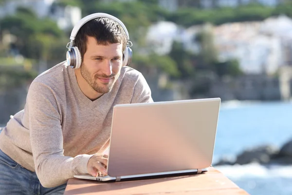 Uomo serio con le cuffie utilizza un computer portatile in un balcone — Foto Stock