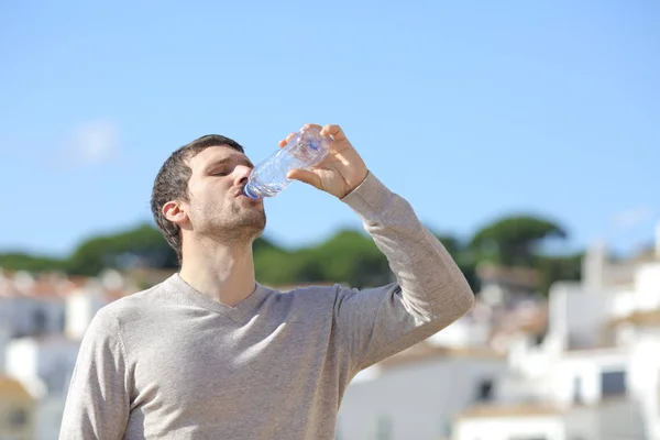 Взрослый мужчина пьет воду в бутылках, стоя в городе — стоковое фото