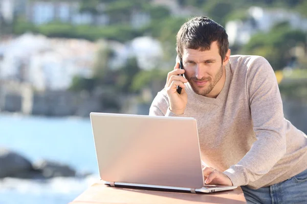 Homem sério usando um laptop e falando ao telefone — Fotografia de Stock