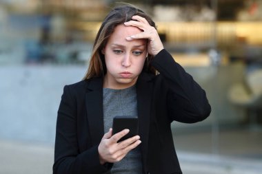 Hüsrana uğramış iş kadını sokakta telefon içeriğini okuyor.