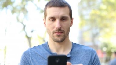 Ciddi bir yetişkin adamın cep telefonuyla kameraya doğru yürüdüğü ön manzara portresi. 