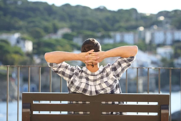 Vue arrière d'un homme reposant assis sur un banc dans une ville côtière — Photo