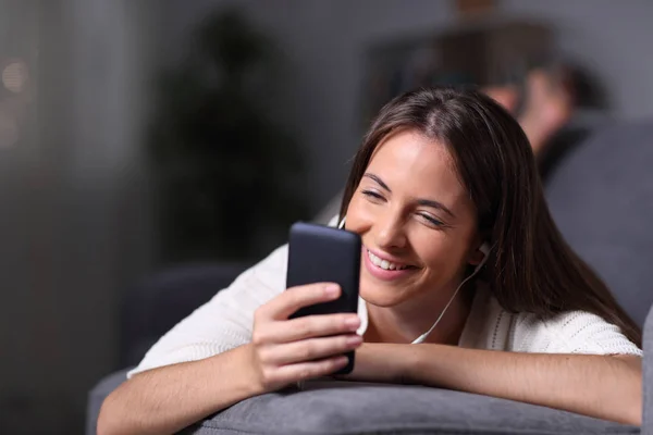 Szczęśliwa nastolatka sprawdza telefon leżący na kanapie w nocy — Zdjęcie stockowe