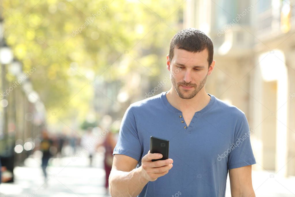Front view of a serious man walking using mobile phone