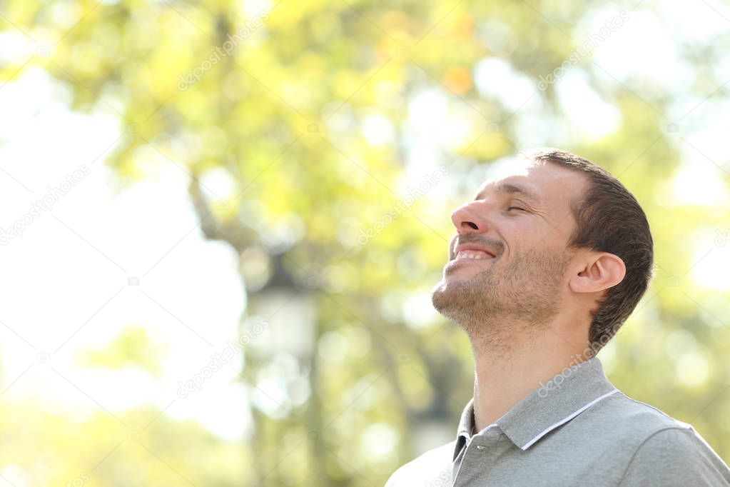 Happy man breathing deep fresh air standing in a park