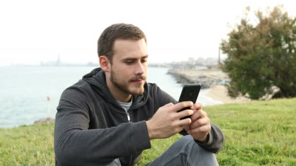 深刻なティーンテキスト上の携帯電話に座っている芝生の上に公園 — ストック動画